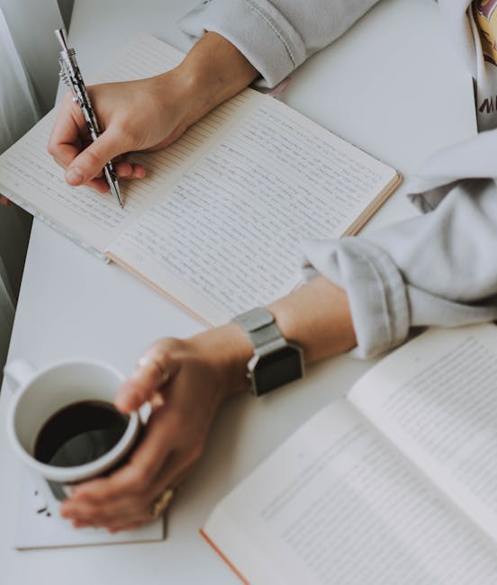 Person Writing on Notebook While Holding Coffee Mug